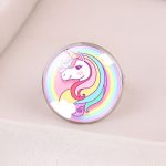 L'image représente une bague en métal avec un cabochon en verre rond. Le cabochon est décoré d'une image d'une licorne blanche avec une crinière et une queue arc-en-ciel. La licorne est entourée de nuages blancs et d'un arc-en-ciel.