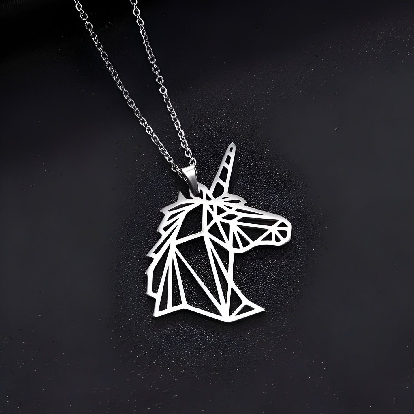 L'image représente un pendentif en forme de tête de licorne en acier inoxydable. La licorne est représentée de profil et est constituée de lignes géométriques. Le pendentif est suspendu à une chaîne en acier inoxydable.