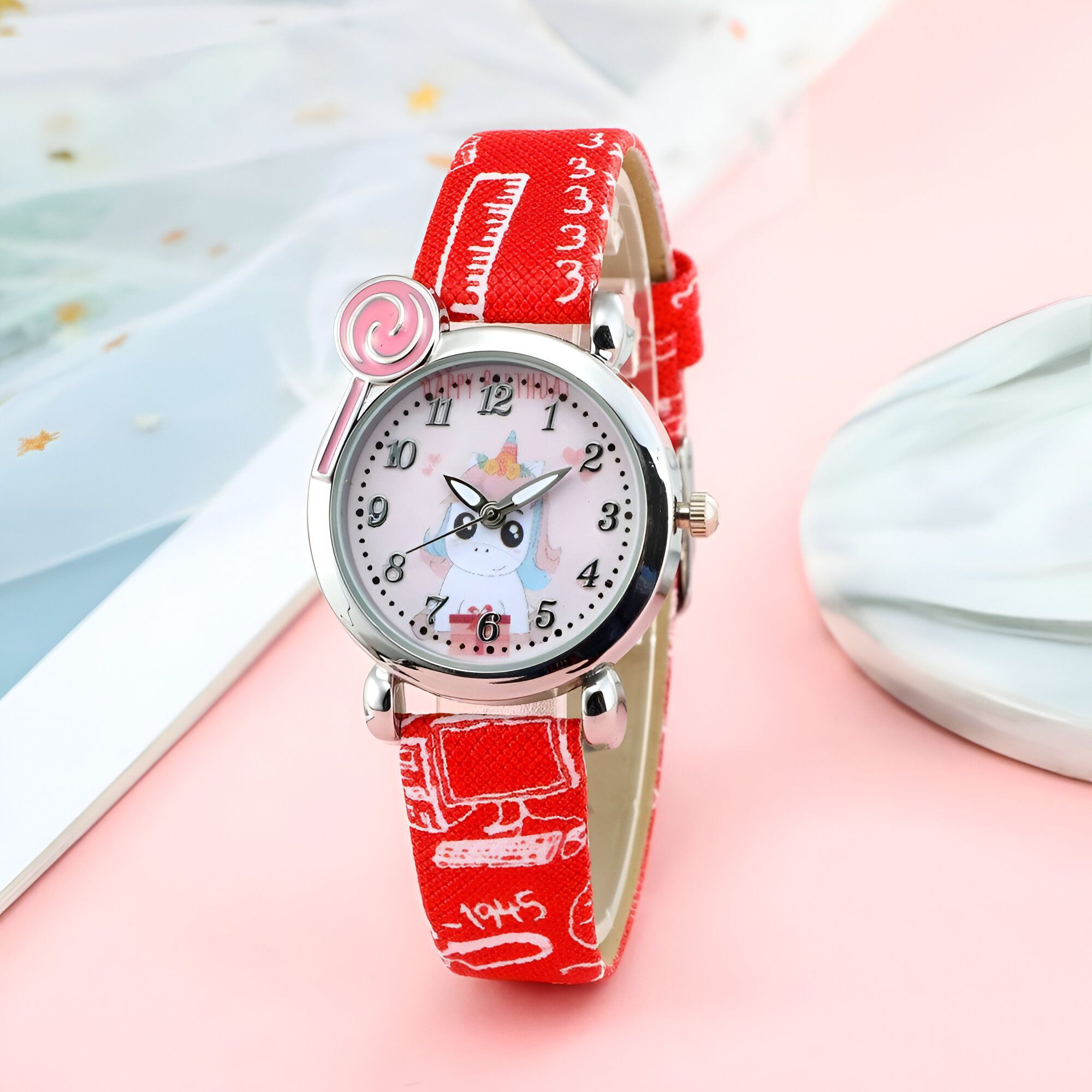 Une montre rouge avec un bracelet en cuir rouge. Le cadran de la montre est blanc avec une image de licorne. Il y a une sucette rose en haut de la montre.