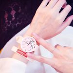 Une personne porte une montre rose avec un lapin blanc dessus. Le bracelet de la montre est blanc avec des écritures rouges "Candycat".