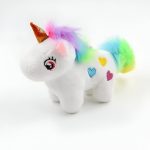 Une peluche de licorne blanche avec une crinière et une queue arc-en-ciel. Elle a une corne dorée et des yeux roses. Il y a des coeurs multicolores sur son corps.